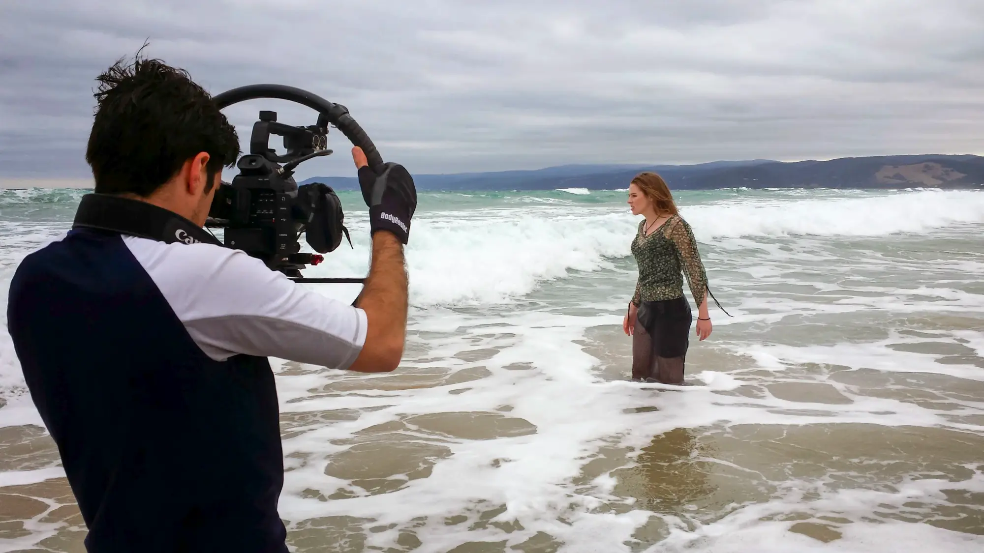 A DCF camera operator filming a singer standing in the surf for a music video